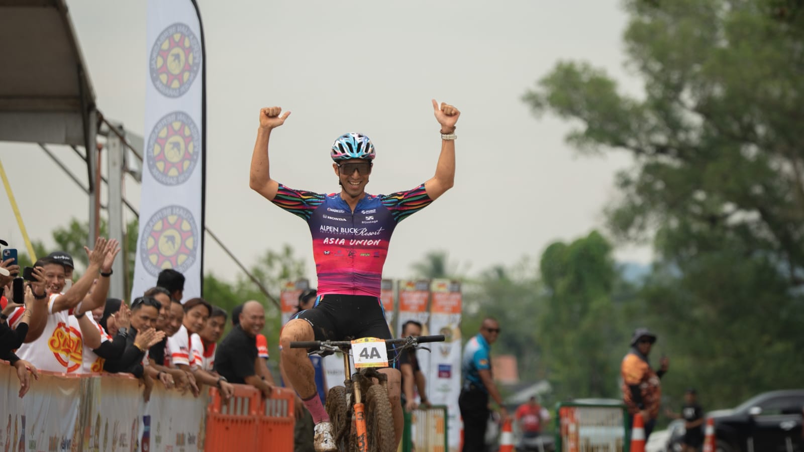 Mountain bike champion celebrating at the finish line with raised arms.